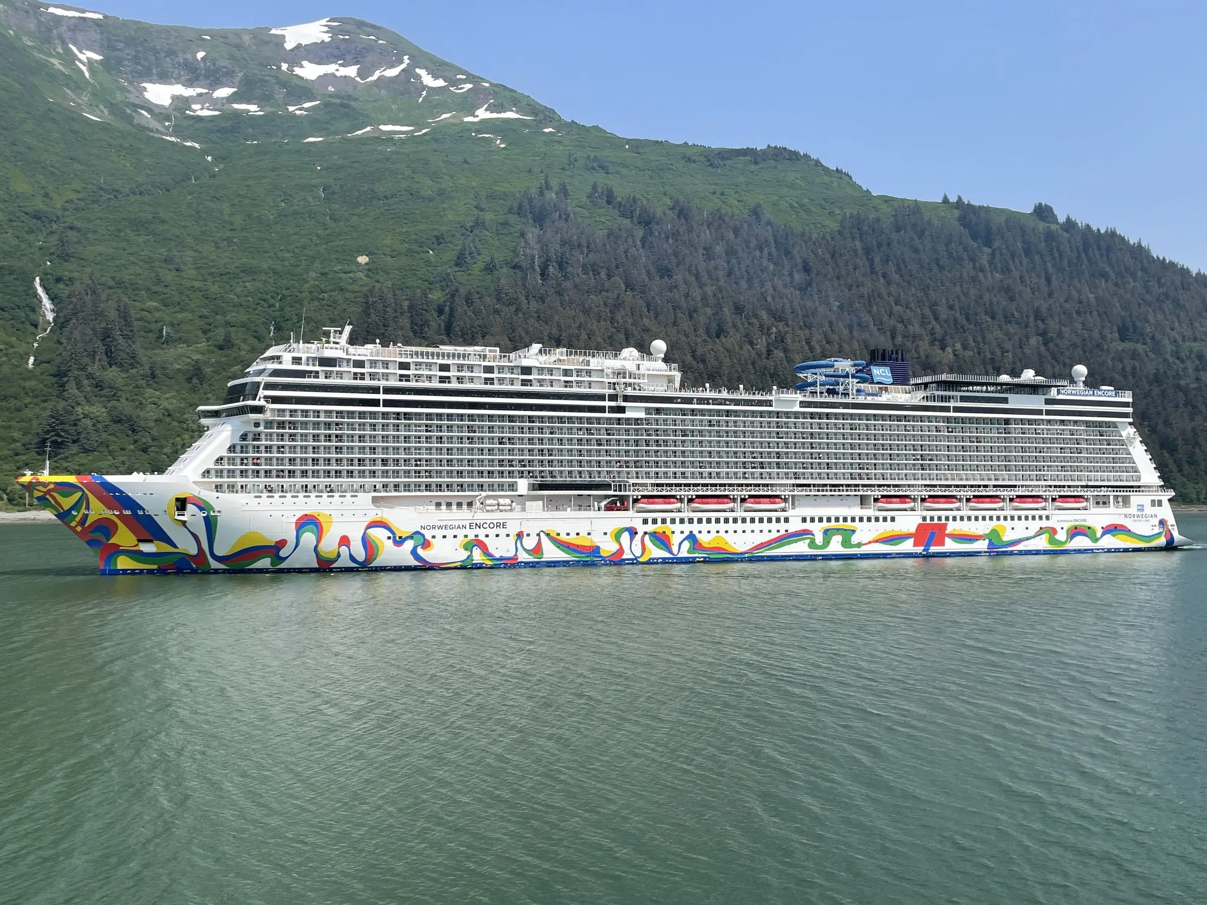 Norwegian Encore side-on in Juneau, Alaska, with its painted hull and forested mountains behind